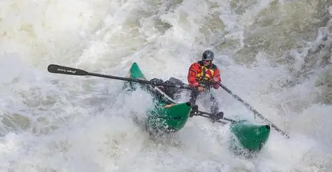 Rower running whitewater in a green cataraft
